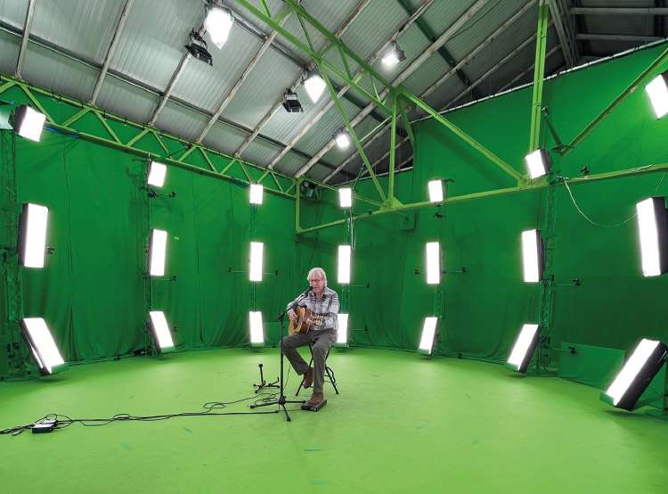 Le chanteur Henri Dès dans un hangar recouvert de fond vert.
